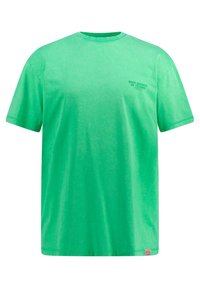 Camiseta de algodón verde con un corte relajado, escote redondo y mangas cortas. Presenta un pequeño texto "SONIDOS PROFUNDOS DEL TECHNO" en el pecho.