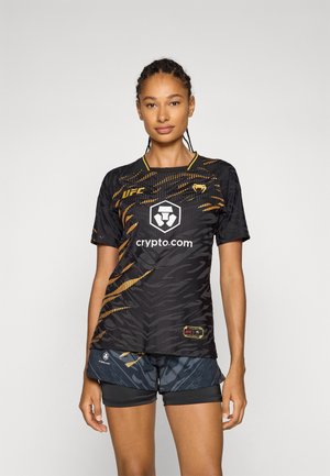 Svart sportsdrakt med gule detaljer, med et tigermønster, logo på brystet og korte ermer. Kombinert med marineblå shorts.