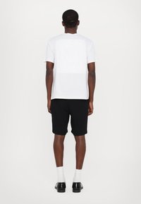 Tricou alb din bumbac cu mâneci scurte, prezintă o grafică mare pe spate; asociat cu pantaloni scurți negri și pantofi negri. Textură netedă, design simplu.
