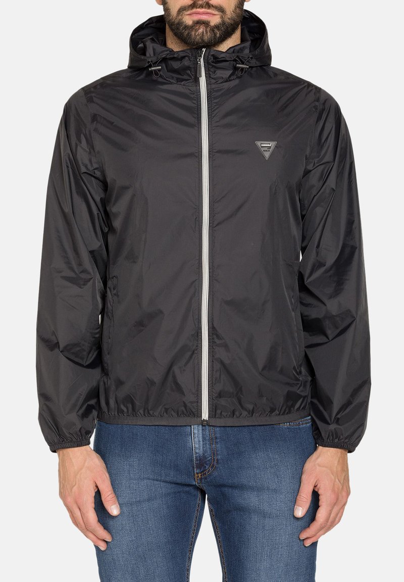 Giacca leggera nera con cappuccio, zip frontale, polsini elastici e patch con logo. Tessuto liscio e materiale resistente al vento.