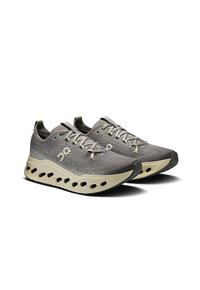 Szare buty sportowe z teksturowaną cholewką, charakteryzujące się unikalnym wzorem podeszwy z dużymi wycięciami, sznurowadłami w pasującym odcieniu szarości oraz subtelnymi akcentami marki.