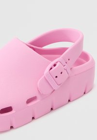 Rosa formade gummiklackar med en texturerad yta, justerbar rem och en tjock plattformssula med utskurna ventilationshål.