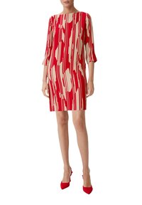 Rotes und beiges Kleid mit geometrischem Muster, knielang, mit Dreiviertelärmeln und geradem Schnitt. Kombiniert mit roten High Heels.