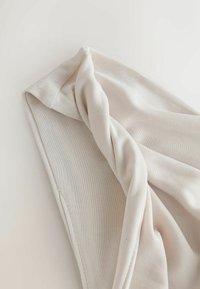 Gros plan d'un tissu beige plié avec une texture tricotée visible et des bords cousus sur un fond clair.