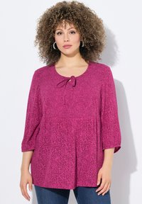 Blusa fucsia con maniche a tre quarti, scollo rotondo e dettaglio con fiocco. Presenta un motivo sottile e una vestibilità ampia e fluida.