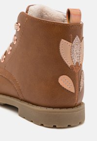 Stivale alla caviglia sintetico marrone con fodera in pelliccia sintetica, occhielli in rame e un motivo floreale decorativo glitterato in tonalità di rosa sul lato.