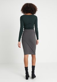 Haut vert foncé à manches longues associé à une jupe grise ajustée, présentant une texture côtelée et une coupe jusqu'aux genoux. Bottines noires complètent la tenue.