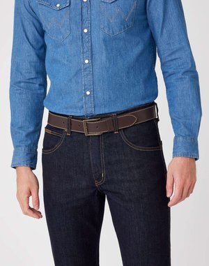 Mann trägt ein blaues Denimhemd, das in dunkle blaue Jeans gesteckt ist, mit einem dunkelbraunen Ledergürtel mit einer metallischen Schnalle.