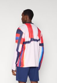 Ilgas rankovėmis marškinėliai su daugiaspalviu abstrakčiu raštu raudonos, mėlynos ir baltos spalvų. Pagaminti iš lengvo audinio, turi apvalią iškirptę.