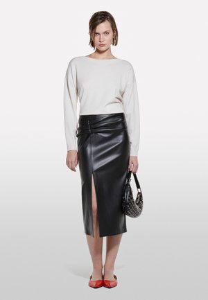 Woman wearing white long-sleeve top, black high-waisted leather skirt with front slit, red shoes, and holding a black studded handbag.