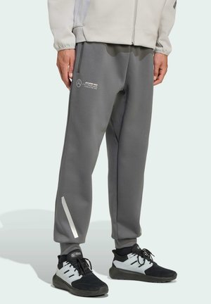 Gray sweatpants made of soft fabric, featuring a white logo, a reflective side stripe, and an elastic waistband. Paired with black sneakers.