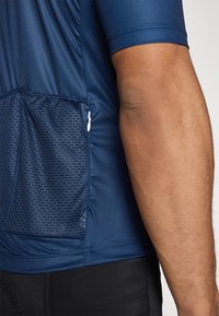 T-shirt de sport navy à manches courtes, avec une poche en maille texturée et une fermeture éclair, fabriqué en matériau synthétique lisse.