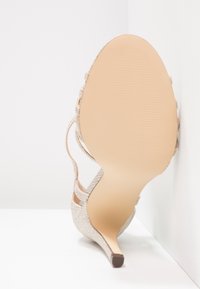 Soulier à talons hauts avec des brides, en argent scintillant, bout pointu et semelle couleur nude. Doté d'un talon mince et effilé.