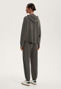 Grå huvtröja med avslappnad passform och sänkta axlar, tillsammans med matchande avsmalnande sweatpants och vita sneakers med gröna detaljer.