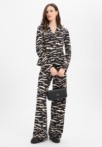 Zwart-beige patroonpak met broekspijpen met wijde pijpen en een nauwsluitend colbert, gecombineerd met een zwarte handtas met gouden accenten.