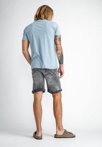 Ljusblå kortärmad skjorta med rund hals, tillsammans med grå denimshorts med uppvikta fållar och en urblekt tvätt. Bruna sandaler.