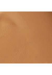 Fond de teint crème dans une teinte chaude, moyen bronzé. Texture lisse et mate avec une application subtile et uniforme, et des imperfections visibles minimales.