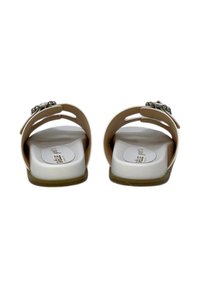 Sandali slip-on beige con suole bianche, dotati di una parte superiore liscia e fibbie decorative. Design aperto e arrotondato che consente il passaggio dell'aria.