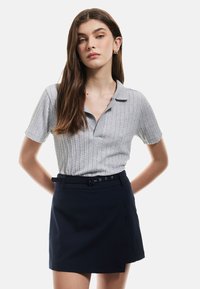 Grå tekstureret polo-shirt med korte ærmer og krave, parret med en marineblå bælteindpakket nederdel. Enkel design, moderne look.