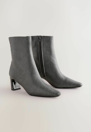 Graue Kunstleder-Ankle Boots mit spitzem Zehenbereich, klobigem schwarzen Absatz und seitlichem Reißverschluss. Glatte Textur und schlankes Design.