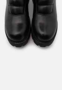 Botas de cuero negro hasta el tobillo con una textura suave, punta redondeada, acentos acolchados y una suela de goma resistente diseñada para la durabilidad.