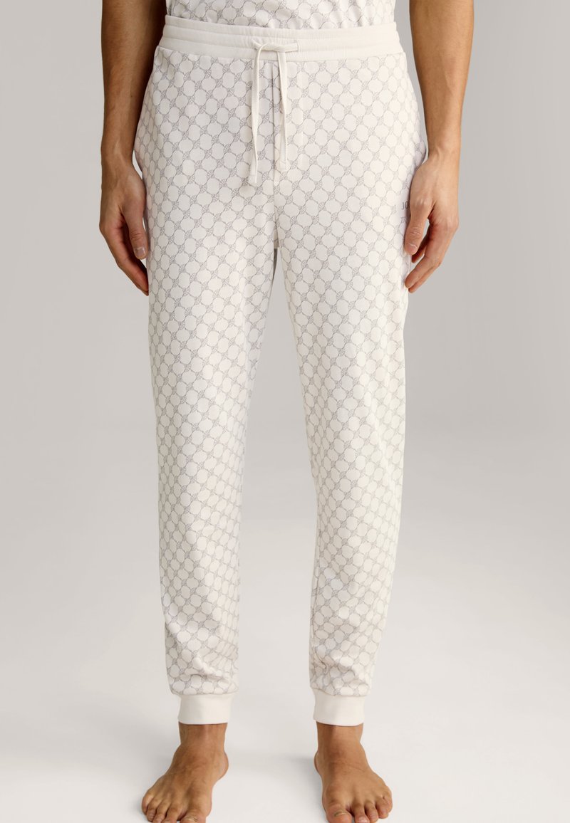 Pantalons de pyjama blancs avec un motif géométrique gris clair, taille élastique avec cordon de serrage, et poignets élastiques aux chevilles. Texture de tissu lisse.