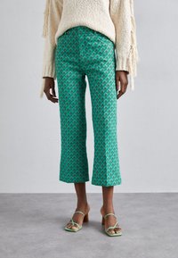 Gröna mönstrade cropped byxor med en diamantdesign, kombinerade med ljusgröna remsandaler och en texturerad krämfärgad tröja.