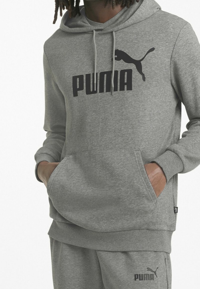 Sudadera gris con un bolsillo frontal, que presenta un gran logotipo negro de "PUMA" y una silueta de puma en negro. Tejido suave y capucha ajustable con cordón.