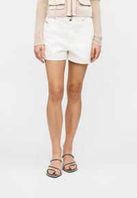 Λευκά βαμβακερά σορτς με λεία υφή, διαθέτουν δύο μπροστινές τσέπες και κλείσιμο με κουμπί. Συνδυάζονται με μαύρα σανδάλια με λουριά.