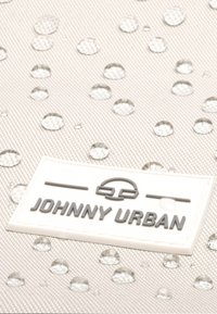 Vizes cseppekkel díszített, világosszürke textúrájú anyag, amelyen egy fehér címke látható, rajta sötétszürke betűkkel "JOHNNY URBAN" felirattal.