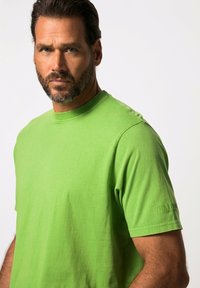 T-shirt verde in cotone con colletto rotondo e maniche corte. Presenta un branding sottile sulla manica sinistra e una texture liscia.