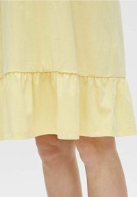 Abito di cotone giallo con orlo a balze svasato, texture morbida, lunghezza al ginocchio e design semplice. Nessun motivo o accessorio visibile.