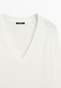 Hvid strikket V-hals sweater med ribbet krave og en mærkat med teksten "Massimo Dutti Made in Madagascar" inde i halsudskæringen.