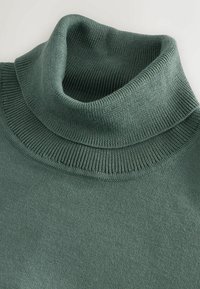 Pulover verde cu guler de tip turtleneck dintr-un material moale, cu o textură și un guler cu nervuri. Vedere de aproape care evidențiază suprafețele netede și forma.