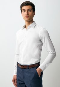 Camicia bianca con bottoni, con colletto strutturato e interno del colletto con motivo. Abbinata a pantaloni blu navy e una cintura in pelle marrone.