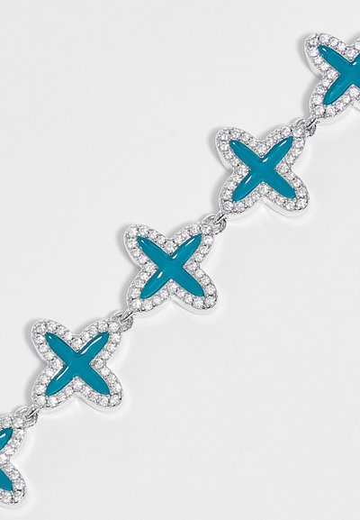 Bracelet chaîne en argent avec des formes de papillons en émail bleu reliées, chacune bordée de petites pierres transparentes sur fond blanc.