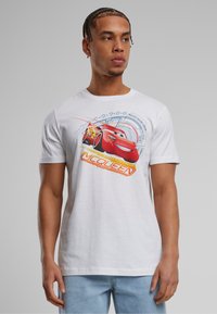 Balta medvilnė marškinėliai su raudonos lenktyninio automobilio "Žaibas McQueen" grafika, mėlynomis ir oranžinėmis detalėmis, apvaliu iškirpimu ir trumpomis rankovėmis.