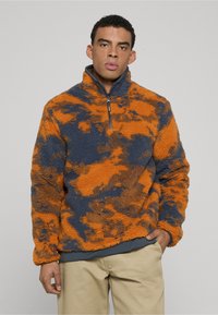 Pullover in pile arancione e blu navy con scollo con mezza cerniera. Presenta un tessuto strutturato con motivo nuvolato e una vestibilità comoda.