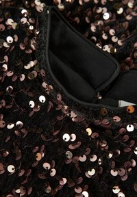 Czarna tkanina z błyszczącymi różowymi cekinami gęsto pokrywającymi powierzchnię, z złożonym kołnierzem wykonanym z gładkiego czarnego materiału.