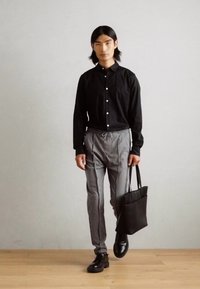 Schwarze Hemd mit Knopfleiste, gestreifte graue Hose und schwarze Schuhe. Hält eine schwarze Tragetasche. Slim Fit, glattes Material und lässiges Design.
