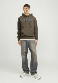 Bruine hoodie met "JACK & JONES" logo, trekkoorden en kangoeroezak, gecombineerd met wijde, vervaagde jeans en zilveren sneakers.