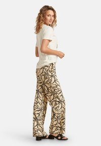 Crème korte mouwen t-shirt gecombineerd met losse beige broek met een zwart bloemenpatroon, aangevuld met zwarte hoge hakken sandalen.
