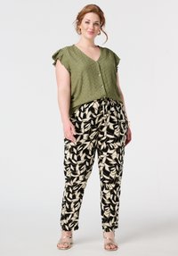 Blouse texturée vert olive avec des manches volantes, associée à un pantalon noir et crème à motifs avec taille à cordon et jambes fuselées.