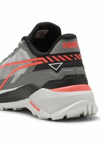 Grijze sneaker met zwarte en neon oranje accenten, met een getextureerde mesh bovenkant, gevoerde kraag en een robuuste witte buitenzool met gripgroeven.