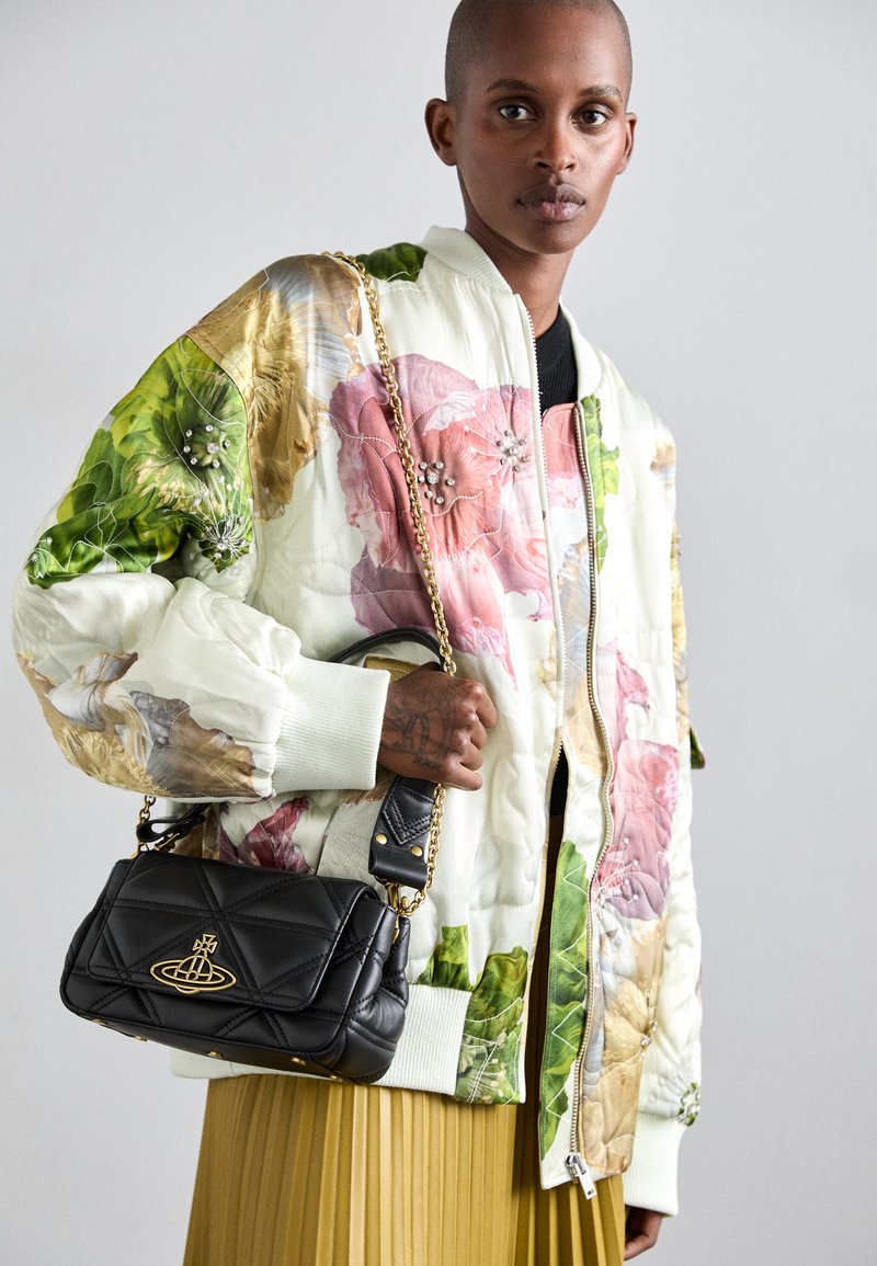 Quilted bomber jacket with floral print in green, pink, and gold. Black mini handbag with chain strap and gold logo. Gold pleated skirt.