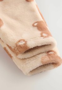 Mjukt, vikt tyg med en beige bakgrund och ljusbruna fläckar, som påminner om ett koschema. Texturen ser plyschig och mysig ut.