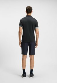 Svart polo skjorta med kontrasterande vita r�änder på ärmarna, parat med marinblå shorts. Tyget ser glatt och lätt ut.
