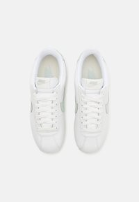 Valged Nike tossud, millel on sile nahkkate, kergete roheliste detailidega, lame pael ja tekstureeritud sisetald. Ringikujulised õmblused on nähtavad.