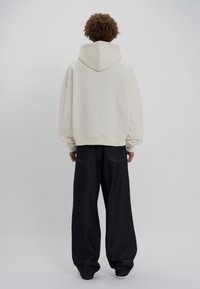 Kremowa, oversize'owa bluza z kapturem na sznurek, zestawiona z ciemnymi, szerokimi spodniami dżinsowymi z tylnymi kieszeniami.