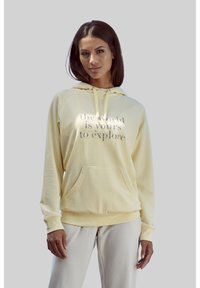Geel hoodie met een voorzak en een trekkoordkap; heeft zilveren tekst met de tekst "de wereld is jouw om te verkennen"; van zacht materiaal.